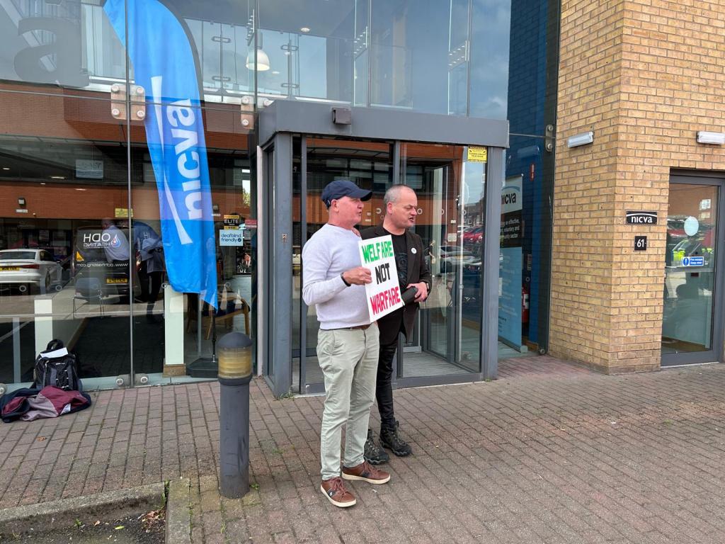 Image shows two people protesting outside the NICVA headquarters
